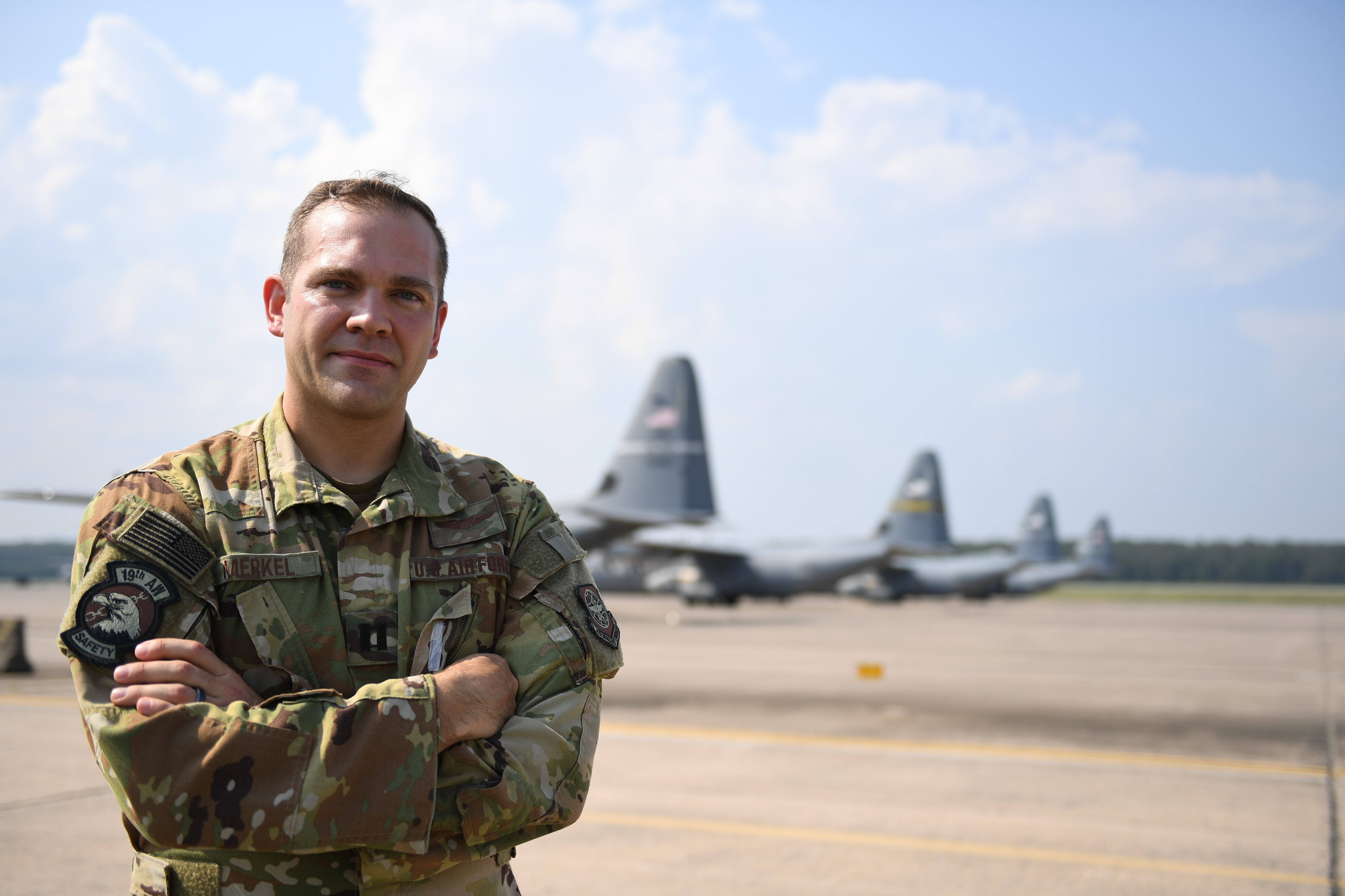 An Air Force officer standing on a flight line with aircraft parked behind him.